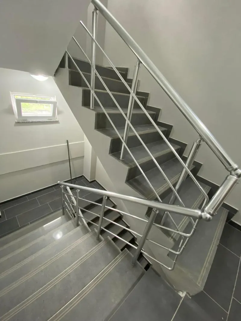 Apartman merdiven boşluğunda iki kat boyunca devam eden parlak alüminyum küpeşte, sahanlıkta dirsekle dönüyor