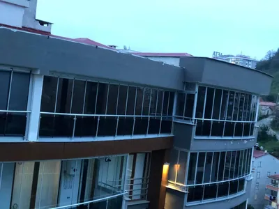 Kavisli apartman cephesinde üst üste üç katın balkonları beyaz profilli katlanır camla kapatılmış