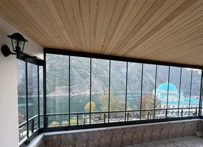 Ahşap tavanlı teras siyah profilli katlanır camla kapatılmış, camların ardında baraj gölü ve cami görülüyor