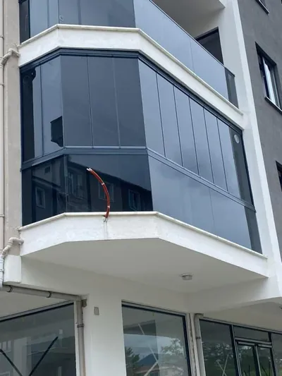 Yeni binanın köşe balkonunu iki cepheden dönen antrasit profilli füme camlı kapatma uygulaması