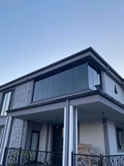 Modern villanın üst kat balkonu antrasit profilli füme camla kapatılmış, köşe dönüşü temiz bitmiş