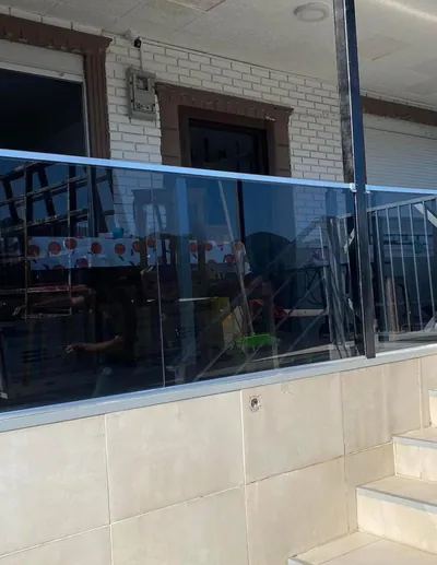Müstakil evin veranda kenarına takılmış füme cam korkuluk, yanında galvaniz merdiven korkuluğu devam ediyor