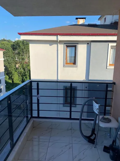 Siyah alüminyum dikme ve yatay borulu füme camlı korkuluk, mermer desenli balkon zemininde köşe dönüyor