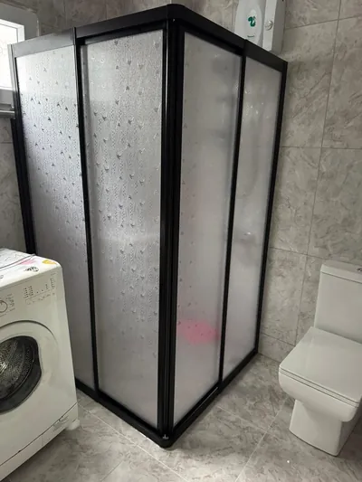 Siyah profilli tam boy köşe duşakabin, yağmur damlası dokulu buzlu camla gri seramik banyoda uygulanmış