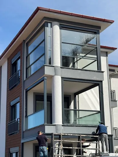 Apartman köşe balkonlarına giyotin cam sisteminin platform üzerinde takıldığı montaj anını gösteren cephe