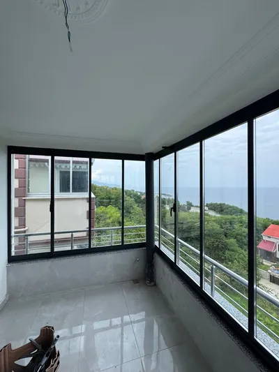 Antrasit profilli köşe balkon iki cepheden açılıyor, bir yanda orman ve deniz diğer yanda komşu bina görülüyor