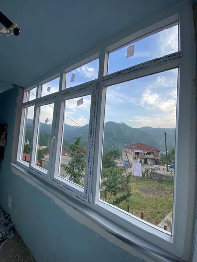 Dört bölmeli beyaz PVC pencere serisi, mavi boyalı odanın tüm duvarını kaplayarak vadiye açılıyor