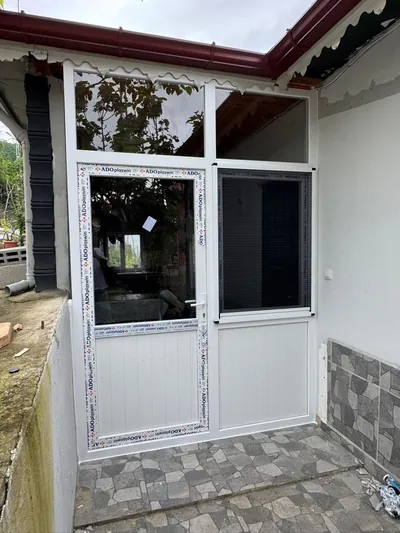 Beyaz PVC giriş kapısı ve yanındaki sineklikli pencere, taş zeminli teras girişine monte edilmiş