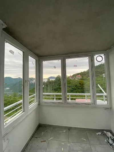 Beyaz PVC doğramayla kapatılmış balkon, köşe dönüşü yaparak vadi ve dağ manzarasını çepeçevre alıyor